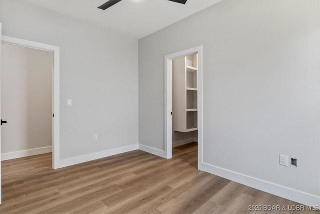 unfurnished bedroom featuring a walk in closet, a closet, light hardwood / wood-style flooring, and ceiling fan