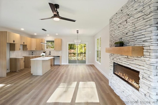 kitchen featuring a stone fireplace, light brown cabinetry, a center island, hanging light fixtures, and light hardwood / wood-style floors