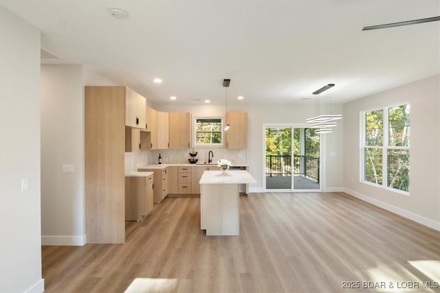 kitchen with light wood-type flooring, backsplash, light brown cabinets, pendant lighting, and a center island