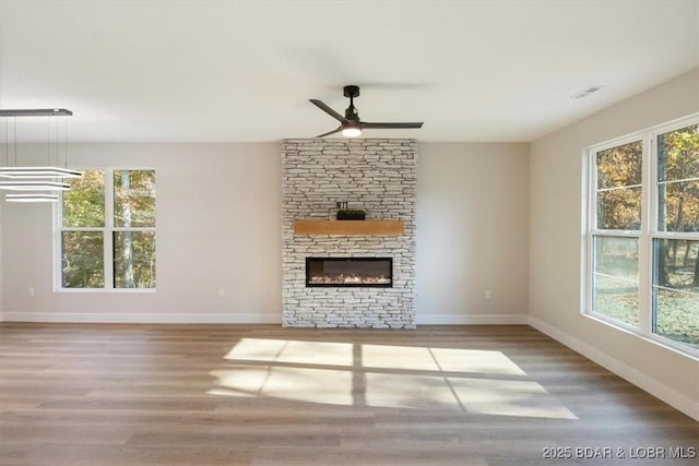 unfurnished living room with a stone fireplace, ceiling fan, and hardwood / wood-style floors