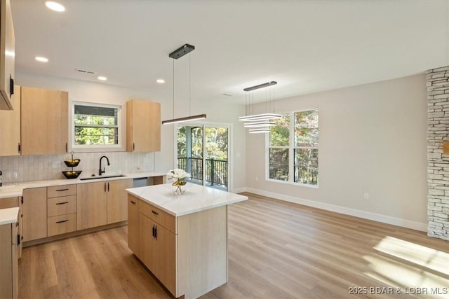 kitchen featuring decorative backsplash, light brown cabinetry, sink, decorative light fixtures, and a kitchen island