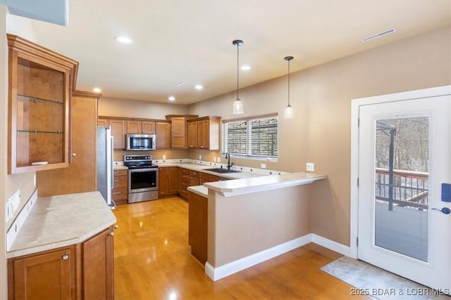 kitchen with kitchen peninsula, appliances with stainless steel finishes, sink, pendant lighting, and light hardwood / wood-style flooring