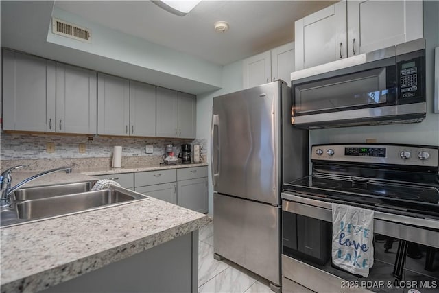 kitchen with appliances with stainless steel finishes, sink, gray cabinetry, and decorative backsplash