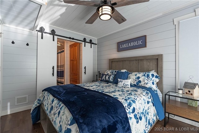 bedroom featuring ceiling fan, a barn door, dark hardwood / wood-style floors, wood walls, and ornamental molding