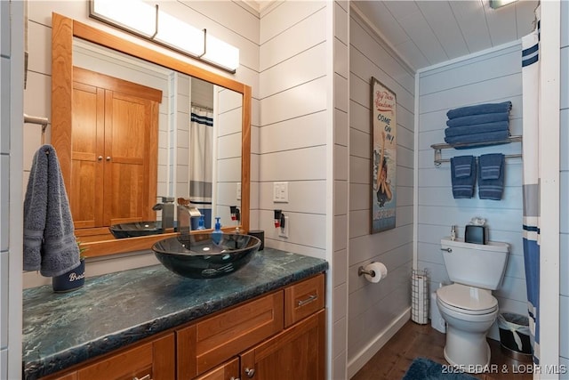 bathroom with wood-type flooring, vanity, toilet, and wood walls