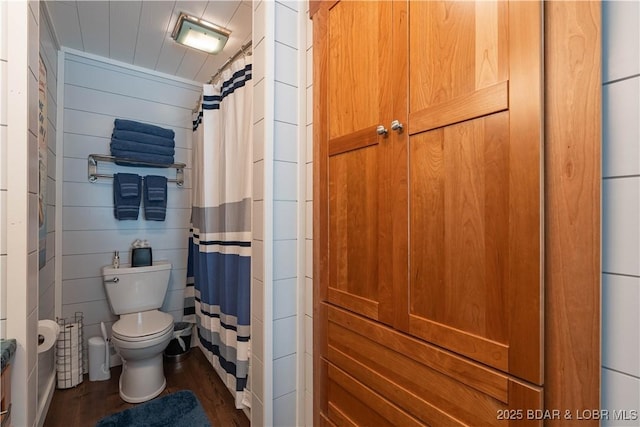 bathroom with hardwood / wood-style floors, a shower with shower curtain, toilet, and wooden walls