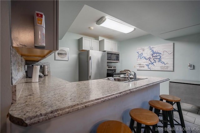 kitchen featuring white cabinetry, sink, stainless steel appliances, kitchen peninsula, and a breakfast bar area