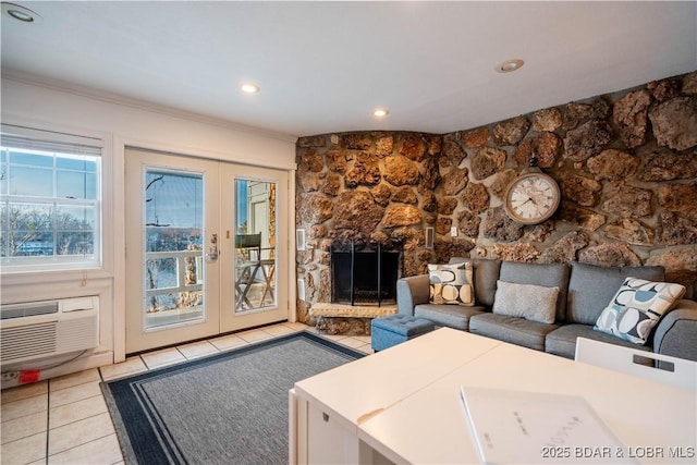 living room with french doors, a stone fireplace, an AC wall unit, light tile patterned floors, and ornamental molding