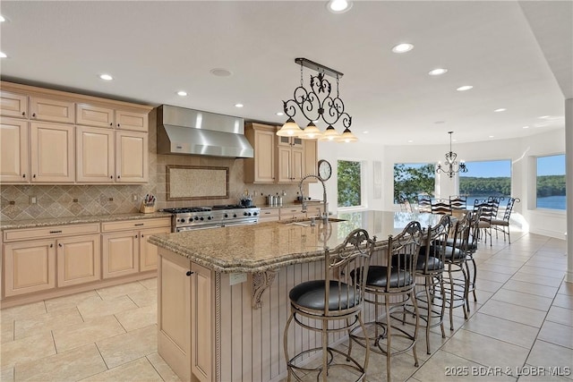 kitchen featuring a center island with sink, a water view, sink, wall chimney exhaust hood, and stainless steel range