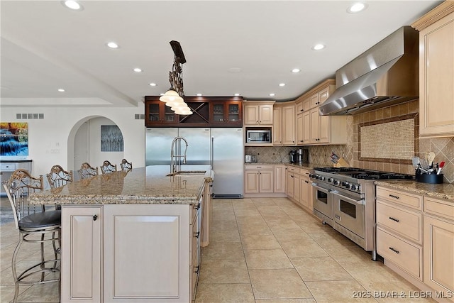 kitchen featuring a center island with sink, a kitchen breakfast bar, wall chimney range hood, and stainless steel appliances