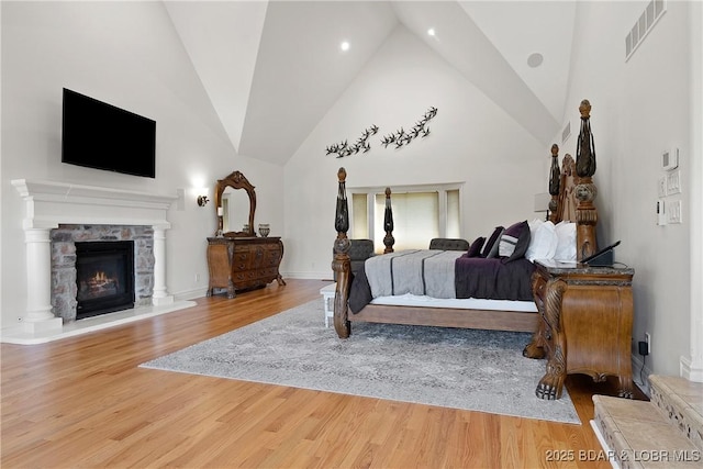 bedroom with hardwood / wood-style flooring, a stone fireplace, and vaulted ceiling