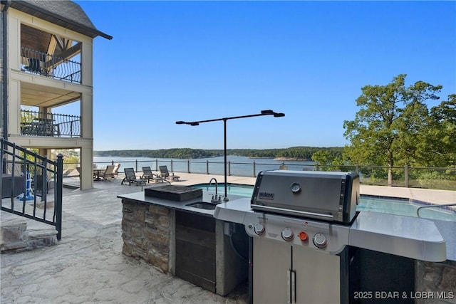 view of patio / terrace with an outdoor wet bar, a balcony, a fenced in pool, area for grilling, and a water view