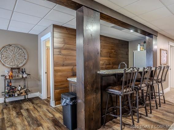 bar with hardwood / wood-style floors, a drop ceiling, white fridge, and light stone counters