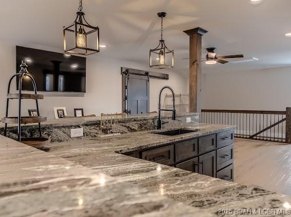 kitchen with ceiling fan, sink, pendant lighting, and light stone counters