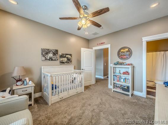 carpeted bedroom with a nursery area and ceiling fan