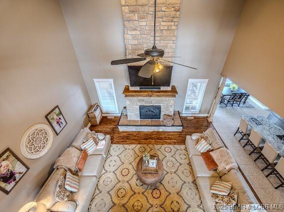 living room with ceiling fan, a stone fireplace, and a towering ceiling