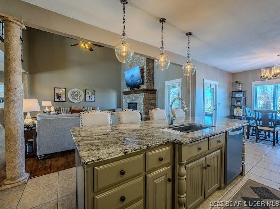 kitchen with a stone fireplace, sink, ornate columns, and a kitchen island with sink