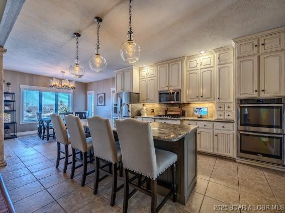 kitchen featuring pendant lighting, cream cabinetry, a kitchen bar, a center island with sink, and appliances with stainless steel finishes