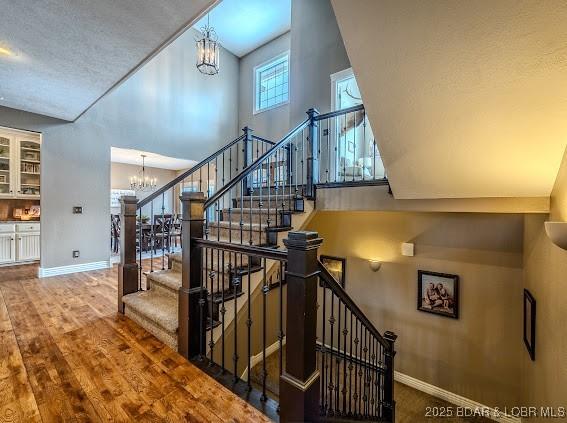 stairway with wood-type flooring, high vaulted ceiling, and a notable chandelier