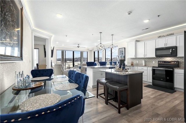 kitchen with electric range, hanging light fixtures, a breakfast bar area, a kitchen island with sink, and white cabinets