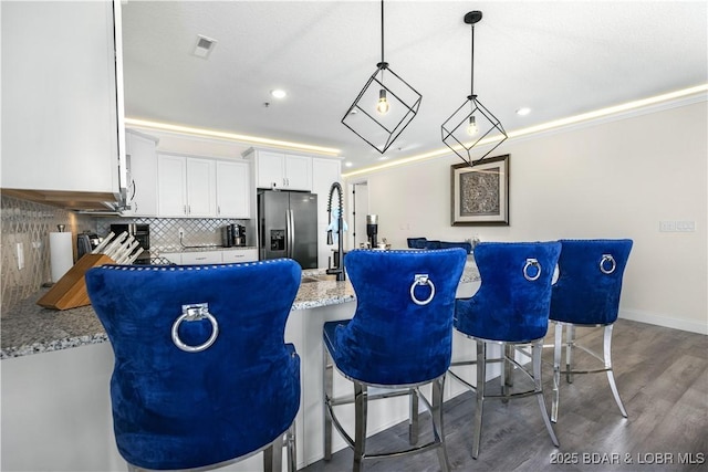 kitchen featuring light stone countertops, stainless steel fridge, backsplash, white cabinetry, and hanging light fixtures