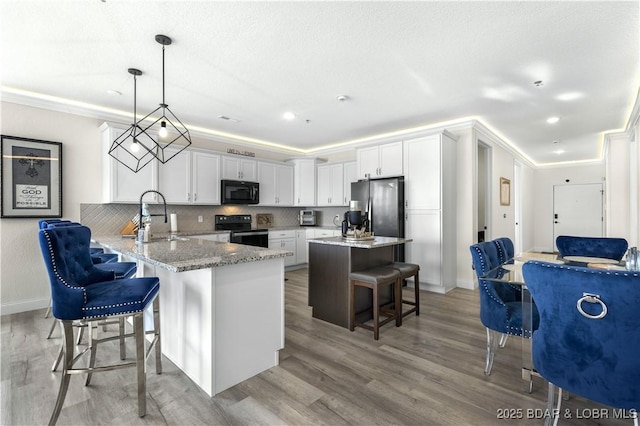 kitchen featuring kitchen peninsula, a kitchen bar, tasteful backsplash, black appliances, and hanging light fixtures