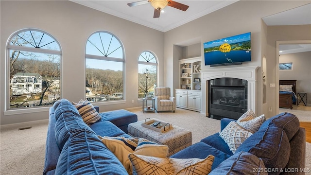 living room with ceiling fan, built in features, carpet floors, and ornamental molding