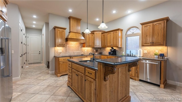 kitchen featuring custom exhaust hood, a center island with sink, hanging light fixtures, sink, and appliances with stainless steel finishes