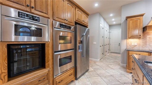 kitchen with stainless steel appliances, tasteful backsplash, wine cooler, dark stone countertops, and light tile patterned floors