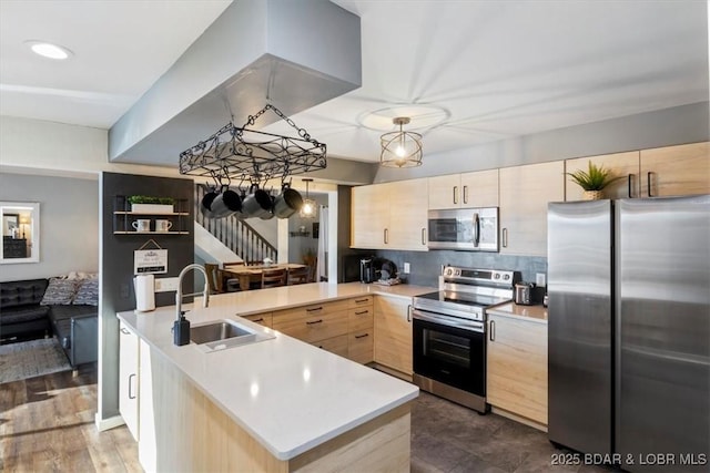 kitchen with light brown cabinetry, sink, hanging light fixtures, appliances with stainless steel finishes, and kitchen peninsula