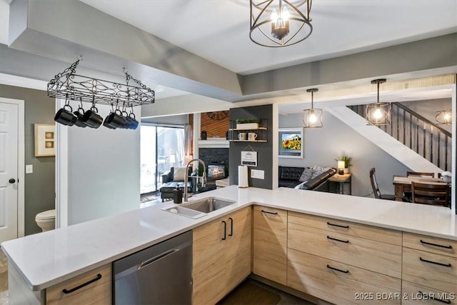 kitchen featuring a fireplace, light brown cabinetry, dishwasher, sink, and kitchen peninsula