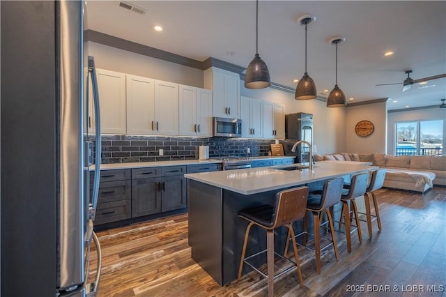 kitchen with hardwood / wood-style floors, white cabinets, crown molding, decorative light fixtures, and stainless steel appliances