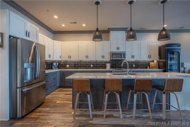 kitchen featuring stainless steel appliances, sink, decorative light fixtures, a center island with sink, and white cabinets