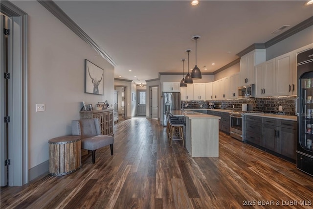 kitchen featuring hanging light fixtures, white cabinets, a breakfast bar area, a kitchen island, and appliances with stainless steel finishes