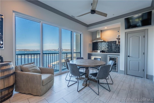 dining room with a water view, wine cooler, ceiling fan, and crown molding