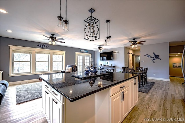 kitchen with decorative light fixtures, white cabinetry, dark stone counters, a center island, and light hardwood / wood-style floors