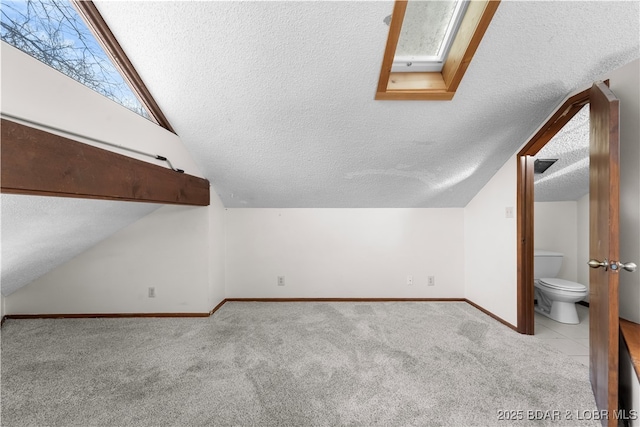 additional living space with vaulted ceiling with skylight, light colored carpet, and a textured ceiling