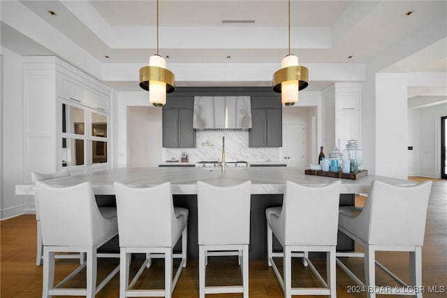 kitchen featuring a raised ceiling, a kitchen bar, decorative light fixtures, and wall chimney range hood