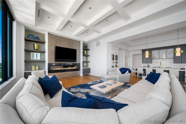 living room featuring built in shelves, beam ceiling, wood-type flooring, and coffered ceiling