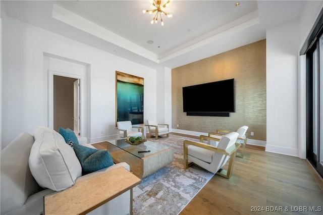 living room featuring a raised ceiling, a chandelier, and light wood-type flooring