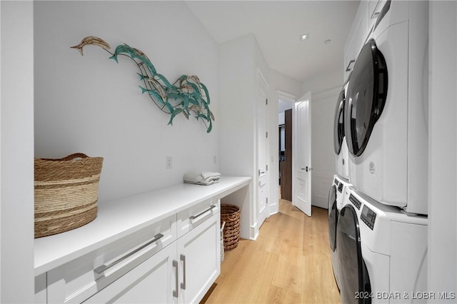 washroom featuring cabinets, light hardwood / wood-style floors, and stacked washer / dryer