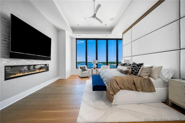 bedroom featuring a raised ceiling, floor to ceiling windows, ceiling fan, and light hardwood / wood-style floors