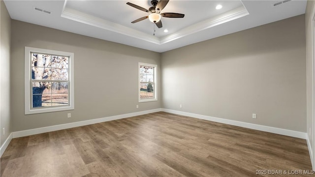 spare room with a tray ceiling, a wealth of natural light, hardwood / wood-style floors, and ceiling fan