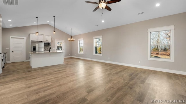 unfurnished living room with light hardwood / wood-style floors, plenty of natural light, lofted ceiling, and ceiling fan with notable chandelier