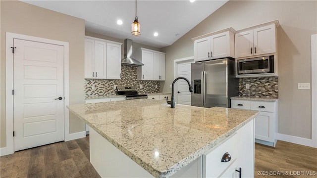 kitchen featuring a center island with sink, wall chimney exhaust hood, lofted ceiling, and appliances with stainless steel finishes