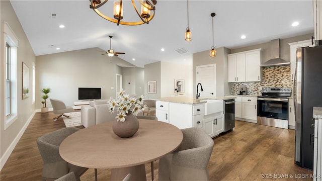 kitchen featuring stainless steel appliances, light stone counters, white cabinets, wall chimney range hood, and lofted ceiling