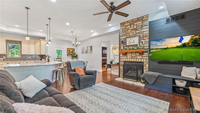 living room featuring ceiling fan with notable chandelier, a raised ceiling, a fireplace, and dark hardwood / wood-style floors