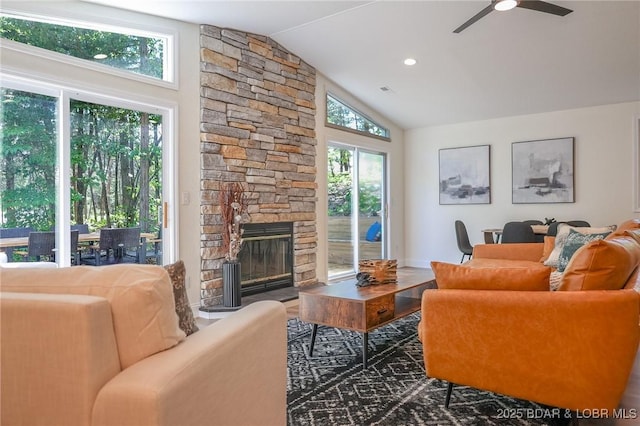 living room featuring lofted ceiling, ceiling fan, and a stone fireplace