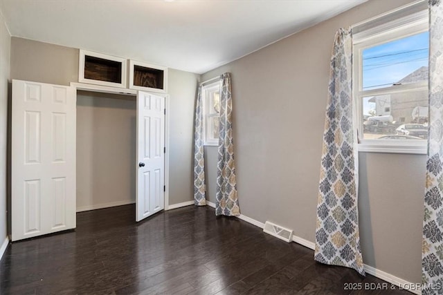 unfurnished bedroom featuring a closet, dark hardwood / wood-style floors, and multiple windows