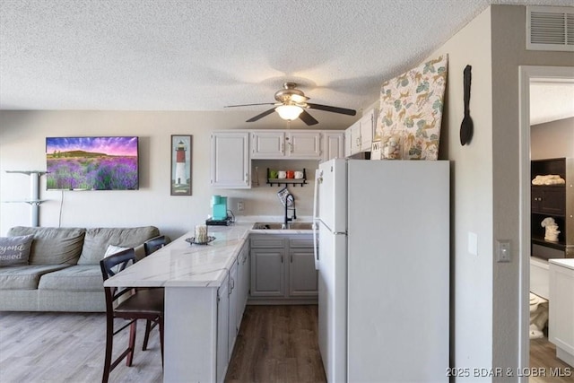 kitchen featuring sink, white cabinetry, white fridge, a kitchen bar, and kitchen peninsula